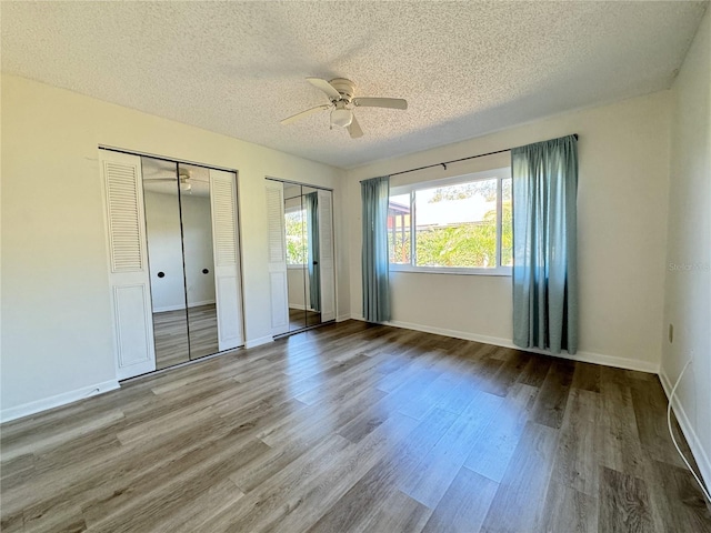 unfurnished bedroom featuring multiple closets, ceiling fan, hardwood / wood-style flooring, and a textured ceiling