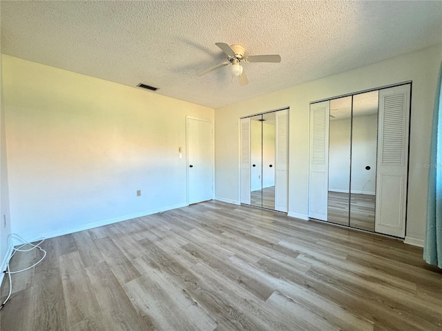 unfurnished bedroom featuring multiple closets, ceiling fan, a textured ceiling, and light wood-type flooring