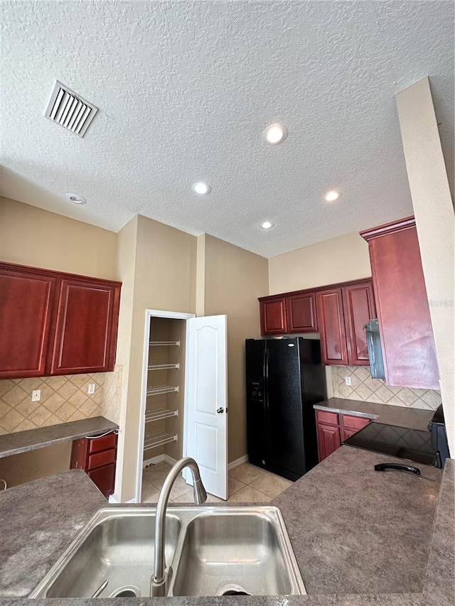 kitchen featuring sink, backsplash, light tile patterned floors, a textured ceiling, and black refrigerator with ice dispenser