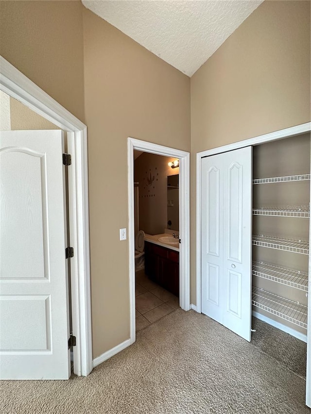 unfurnished bedroom featuring sink, ensuite bath, a textured ceiling, carpet floors, and a closet