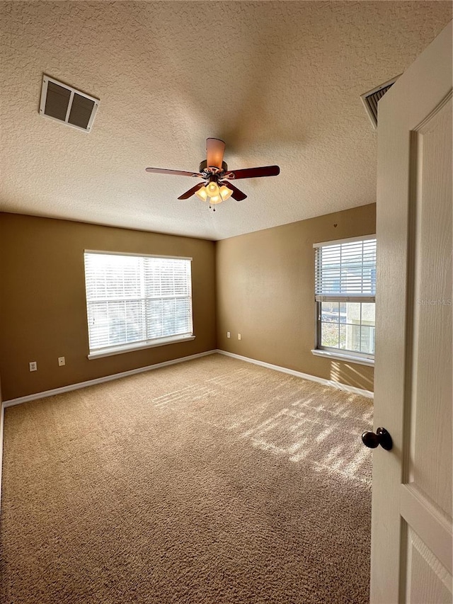 carpeted empty room featuring ceiling fan, a textured ceiling, and a healthy amount of sunlight