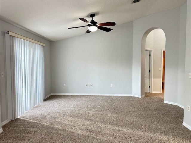 empty room featuring carpet flooring, baseboards, ceiling fan, and arched walkways