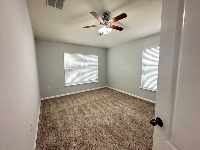 empty room with carpet, a ceiling fan, visible vents, and a wealth of natural light