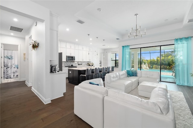 living room featuring a chandelier, dark hardwood / wood-style flooring, and a tray ceiling