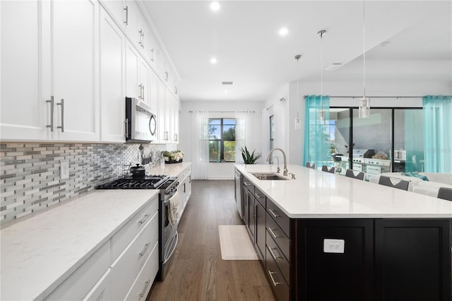 kitchen with appliances with stainless steel finishes, sink, white cabinets, hanging light fixtures, and a kitchen island with sink