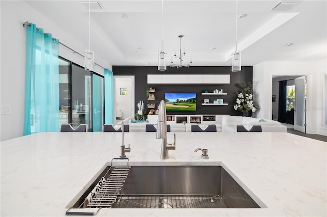 kitchen featuring hanging light fixtures, sink, light stone counters, and a tray ceiling