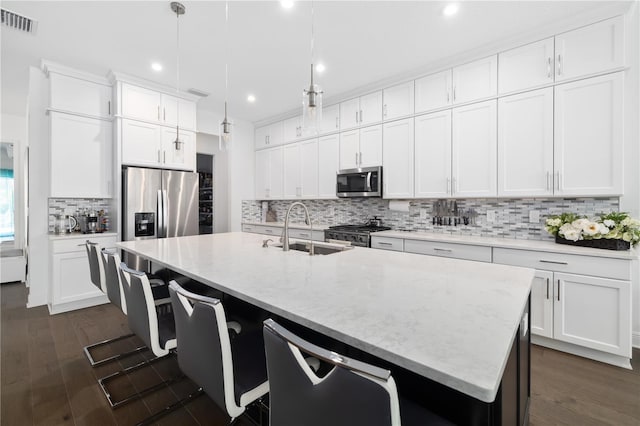 kitchen featuring hanging light fixtures, stainless steel appliances, sink, and a center island with sink