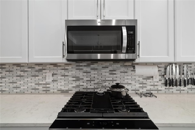 details featuring light stone counters, backsplash, stovetop, and white cabinets