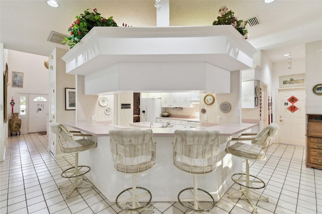 kitchen featuring white fridge with ice dispenser, a kitchen bar, white cabinetry, and kitchen peninsula