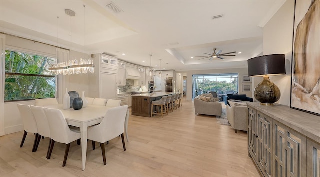 dining space with a raised ceiling, ceiling fan, and light hardwood / wood-style flooring