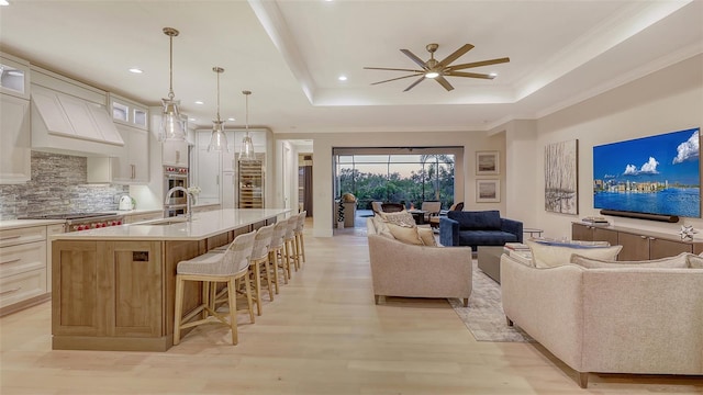 kitchen with a kitchen island with sink, pendant lighting, a kitchen bar, and a tray ceiling