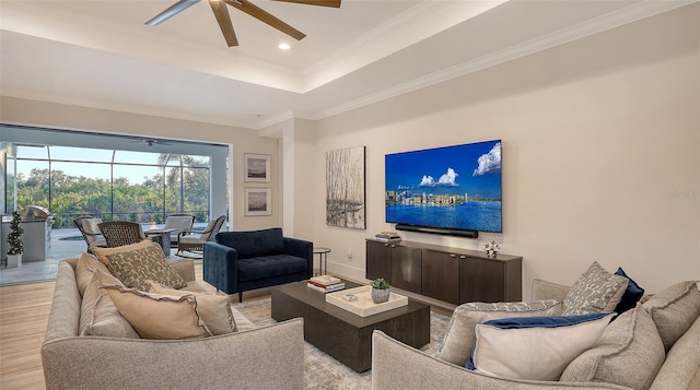 living room featuring ceiling fan, ornamental molding, a tray ceiling, and light hardwood / wood-style floors