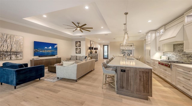 living room featuring a raised ceiling, sink, ceiling fan, and light hardwood / wood-style flooring