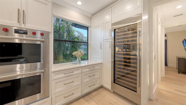 kitchen with double oven, beverage cooler, white cabinets, and light wood-type flooring