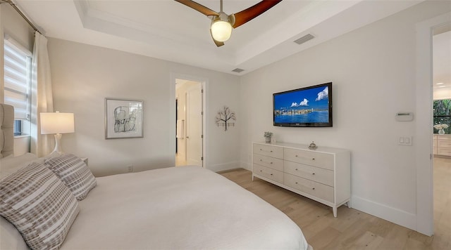 bedroom with ceiling fan, a tray ceiling, and light wood-type flooring