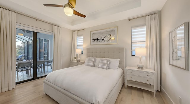 bedroom featuring ceiling fan, a tray ceiling, light hardwood / wood-style floors, and access to exterior