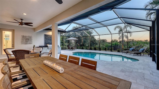 pool at dusk with exterior kitchen, a patio, a lanai, and ceiling fan