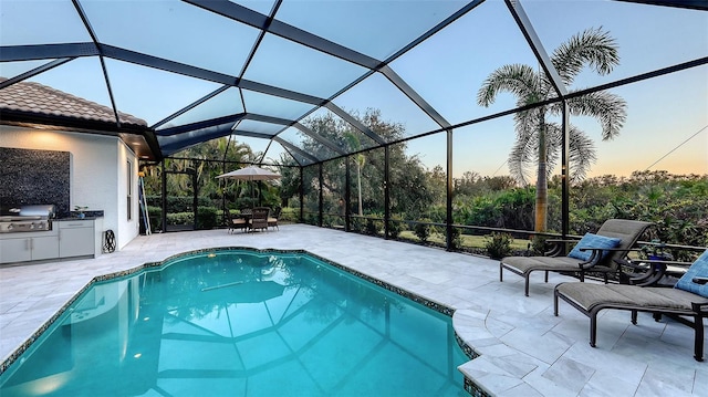 pool at dusk with a lanai, a patio area, grilling area, and an outdoor kitchen