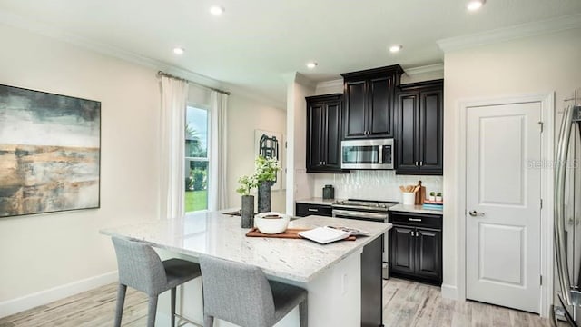 kitchen with a breakfast bar, light stone counters, a kitchen island with sink, stainless steel appliances, and light hardwood / wood-style floors