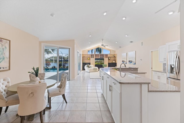 kitchen featuring light stone counters, lofted ceiling, white cabinets, and a center island with sink