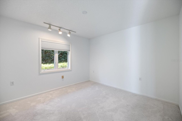 empty room featuring track lighting, light colored carpet, and a textured ceiling