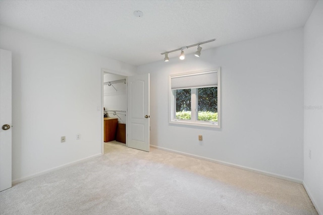 unfurnished bedroom with a spacious closet, a textured ceiling, track lighting, a closet, and light colored carpet