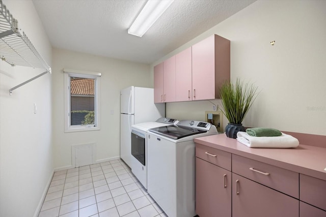 clothes washing area with cabinets, washing machine and dryer, light tile patterned floors, and a textured ceiling