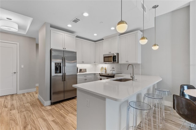 kitchen with pendant lighting, sink, stainless steel appliances, white cabinets, and kitchen peninsula