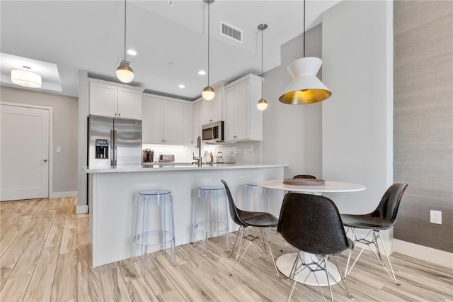 kitchen featuring hanging light fixtures, stainless steel appliances, kitchen peninsula, and white cabinets