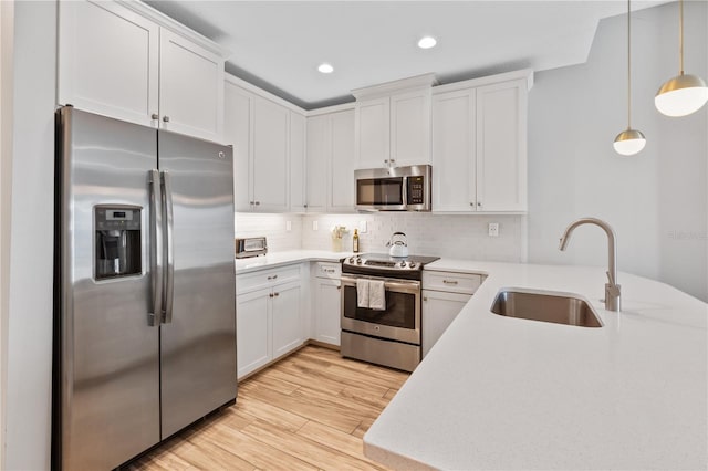 kitchen with pendant lighting, sink, stainless steel appliances, light hardwood / wood-style floors, and white cabinets