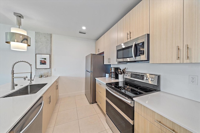 kitchen featuring light tile patterned floors, sink, appliances with stainless steel finishes, hanging light fixtures, and light brown cabinets