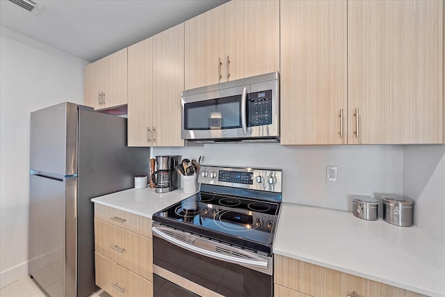 kitchen with light brown cabinetry, light tile patterned floors, and stainless steel appliances