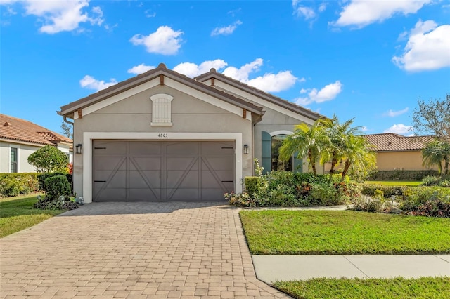 view of front facade with decorative driveway, an attached garage, a front yard, and stucco siding