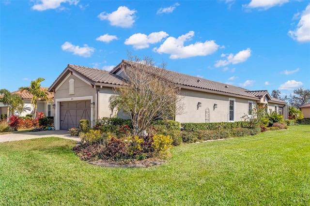 view of side of home with a garage, driveway, a tile roof, a yard, and stucco siding