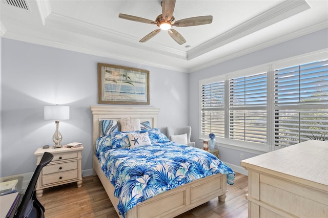 bedroom with crown molding, a raised ceiling, visible vents, ceiling fan, and wood finished floors