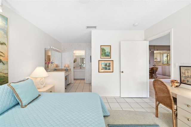 bedroom featuring light tile patterned flooring, a textured ceiling, ensuite bathroom, and visible vents