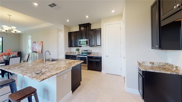 kitchen featuring appliances with stainless steel finishes, a kitchen island with sink, sink, and light stone countertops