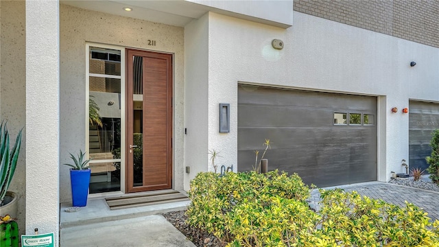 view of exterior entry with a garage and stucco siding