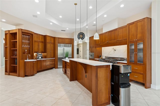13315 Palmers Creek Ter, Lakewood Ranch, FL 34202 - kitchen with a kitchen island with sink, backsplash, hanging light fixtures, built in appliances, and a raised ceiling