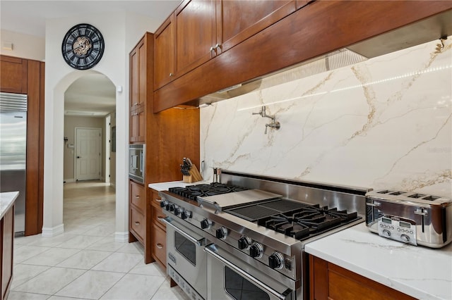 13315 Palmers Creek Ter, Lakewood Ranch, FL 34202 - kitchen with range hood, tasteful backsplash, built in appliances, light tile patterned floors, and light stone counters