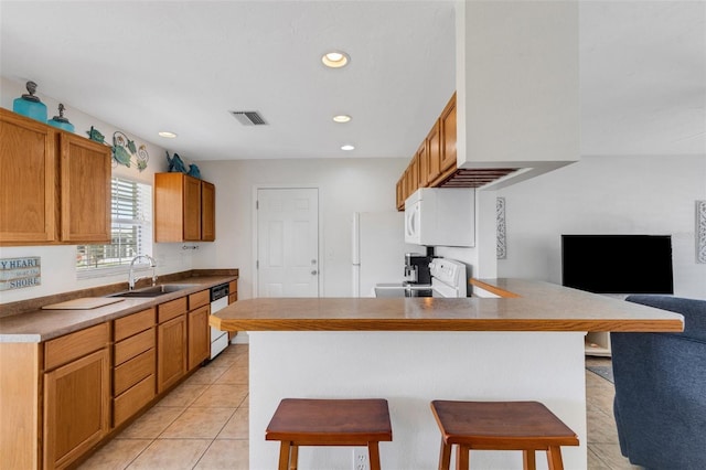 kitchen with sink, white appliances, light tile patterned floors, a kitchen bar, and kitchen peninsula