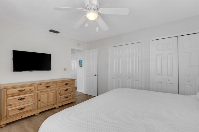 bedroom with multiple closets, hardwood / wood-style flooring, and ceiling fan