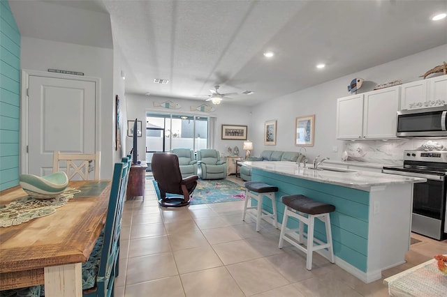 kitchen with an island with sink, white cabinets, backsplash, stainless steel appliances, and light stone countertops