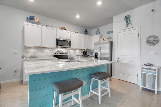 kitchen with tasteful backsplash, an island with sink, appliances with stainless steel finishes, and white cabinets