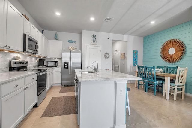 kitchen featuring a breakfast bar, sink, white cabinetry, appliances with stainless steel finishes, and an island with sink