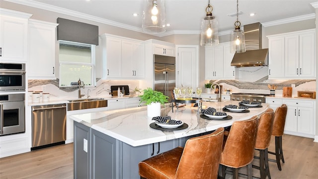 kitchen featuring stainless steel appliances, a kitchen island with sink, wall chimney range hood, and white cabinets