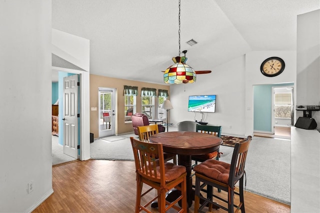 dining area featuring wood-type flooring, vaulted ceiling, and a textured ceiling