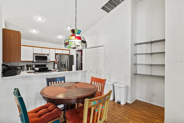 dining room featuring light hardwood / wood-style flooring, a textured ceiling, and vaulted ceiling