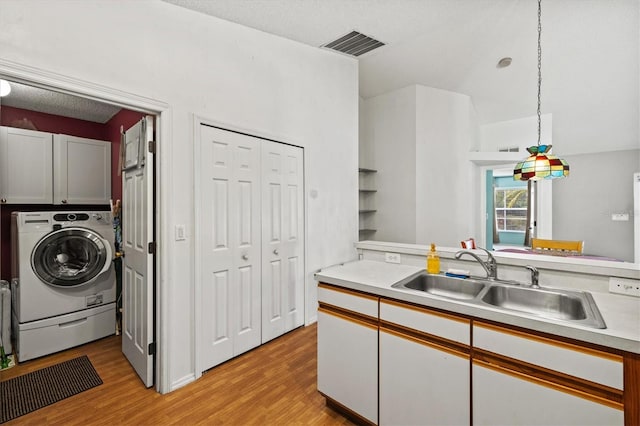 kitchen featuring pendant lighting, sink, light hardwood / wood-style flooring, white cabinetry, and washer / dryer