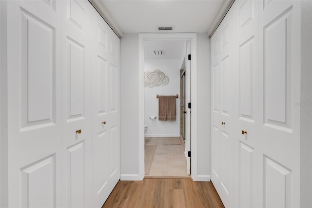 corridor with baseboards, visible vents, and light wood finished floors